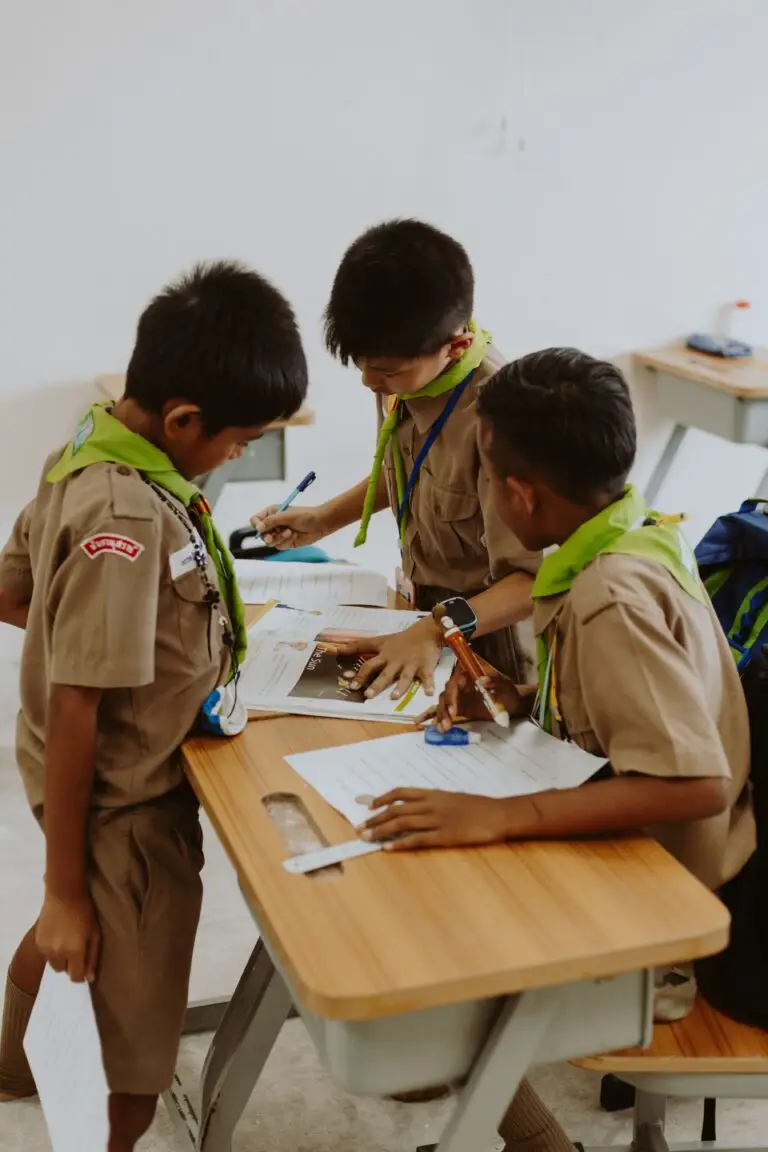 Home Children in school uniforms working together at a desk in a classroom.
