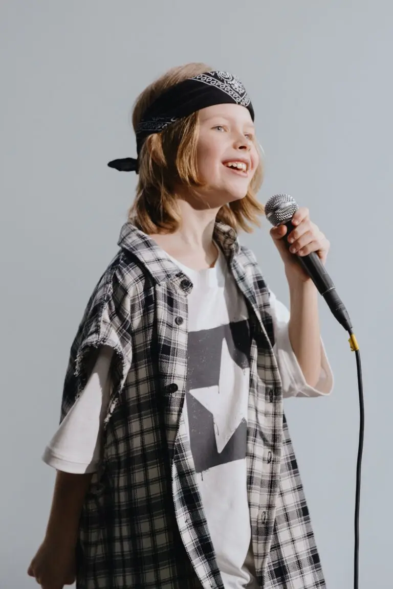 Home A young girl holding a microphone and singing with enthusiasm, wearing a plaid shirt and bandana.